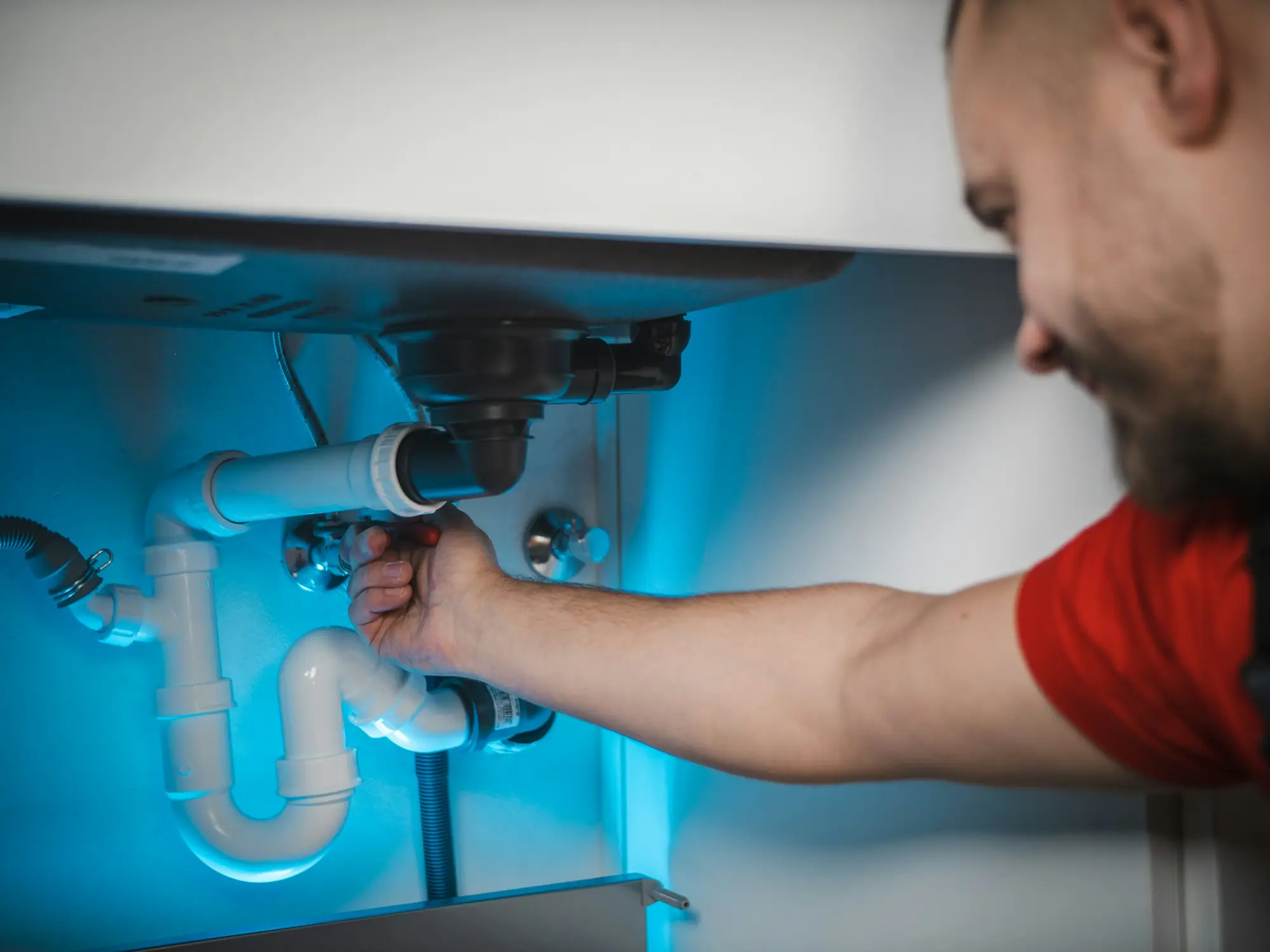 Plombier resserrant un raccord sous un lavabo